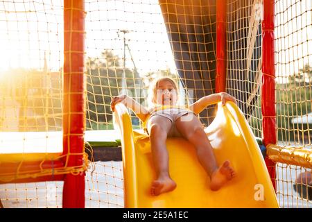 Una ragazza felice divertente carina si siede su un giallo luminoso scivola in un variopinto centro di intrattenimento e preparati a scendere in una giornata di sole Foto Stock