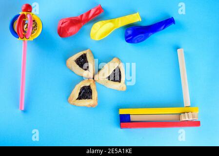 Hamantaschen biscotti o amans orecchie, legno colorato noisemakers e palloncini per Purim celebrazione ebraico carnevale vacanza su sfondo blu.Top view.Flat Lay. Foto Stock
