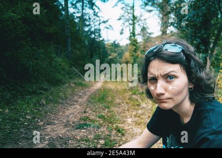 Ritratto di una ragazza dagli occhi blu che guarda la macchina fotografica e fa divertimento con crema solare sul viso in natura Foto Stock