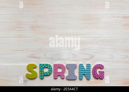 Parola PRIMAVERA di colorate lettere in legno su sfondo bianco dipinto vintage in legno con spazio copia. Concetto di primavera e stagioni. Vista dall'alto Foto Stock