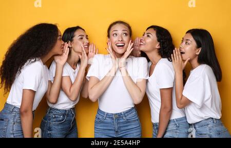 Eccitato giovani Donne gossiping condividere voci e segreti, sfondo giallo Foto Stock