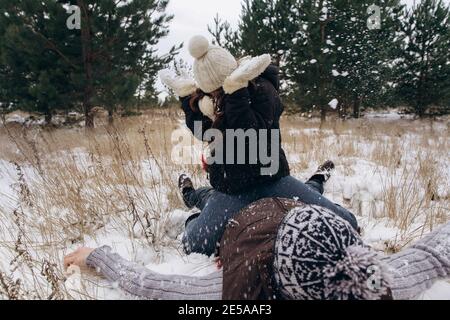 La donna si siede sull'uomo. Coppia che gioca a palle di neve in un campo invernale innevato. Foto Stock