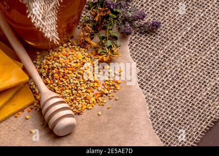 Miele in vaso con cucchiaia di miele, polline di cera d'api e fiori secchi su sfondo di legno d'annata Foto Stock