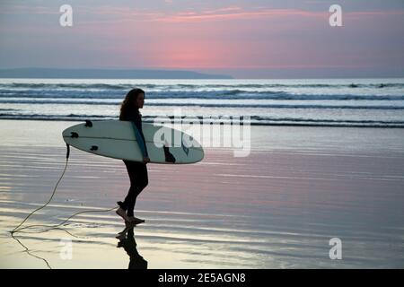 Surfista femminile con surf in mare per una serata di surf a Westward ho!, North Devon, Inghilterra Foto Stock