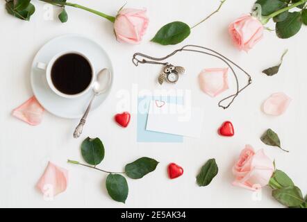 San Valentino sfondo giorno - tazza di caffè, rose di pesca, carta bianca, orologio a forma di gufo, caramelle a forma di cuore su sfondo bianco Foto Stock