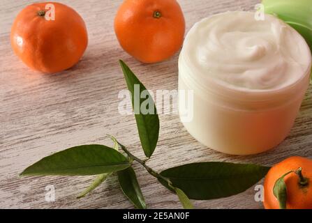 Crema naturale di pelle con estratto di mandarino con frutta e foglie su tavola di legno. Vista rialzata. Foto Stock