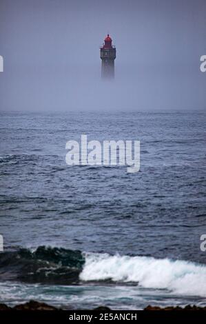 Il drammatico faro la Jument, circondato dalla nebbia estiva, al largo della costa dell'Ile d'Ouessant, Bretagna. L'iconico faro alto 47 metri era bui