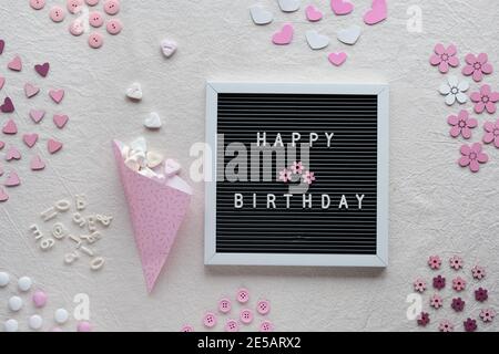 Invia un SMS di buon compleanno su una lavagna a lettere, una lavagna a lettere o un tabellone. Disposizione piatta, vista dall'alto con scatola luminosa su avorio, tessuto bianco. Cuori rosa, caramelle Foto Stock