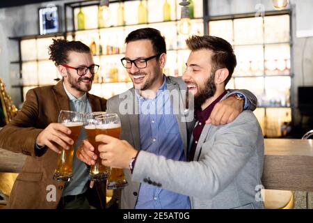 Giovani uomini d'affari bevono birra, parlano e sorridono mentre riposano al pub Foto Stock