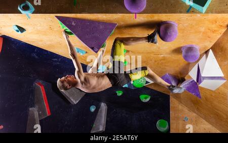 Giovane uomo bouldering in piscina palestra di arrampicata, cercando di risolvere il problema stimolante Foto Stock