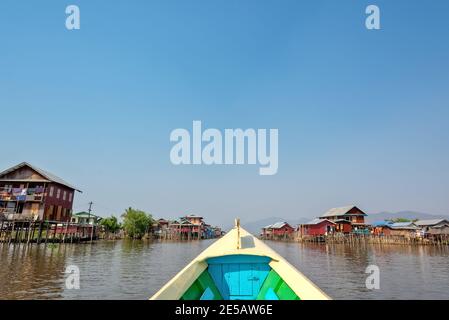 Barca che arriva in un colorato villaggio galleggiante con palafitte in Birmania, Myanmar Foto Stock