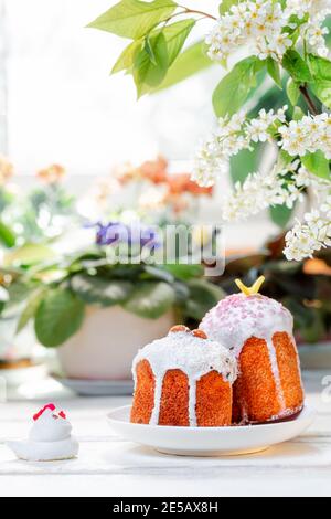 Vacanze di Pasqua. Due pane pasquale decorato su un piatto accanto a una figurina di pollo. Sullo sfondo, piante e fiori. Orientamento verticale. Foto Stock