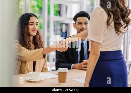 Closeup handshake dopo intervista accordo tra giovane donna asiatica e due manager con movimento positivo in sala riunioni, handshake con manager, Bu Foto Stock