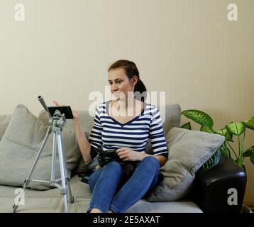 Un primo piano di una giovane donna felice che registra un video utilizzando un telefono in piedi su un treppiede, un blogger sorridente che scatta un video per un canale, video bl Foto Stock