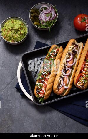 Gourmet panino hot dog sporco con varie guarnitura su sfondo di pietra nera. Opzione sana di fast food. Foto Stock