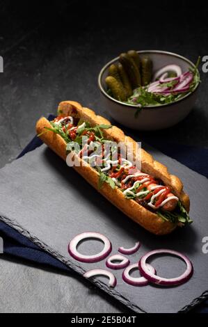 Gourmet panino hot dog sporco con varie guarnitura su sfondo di pietra nera. Opzione sana di fast food. Foto Stock