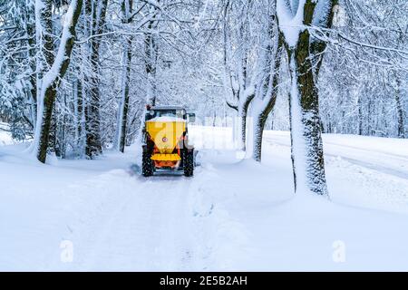 Trattore con spanditore di sale montato, manutenzione stradale - veicolo con dispositivo di sgranamento invernale. Trattore che sghiaccia la strada, spandendo il sale. Servizio municipale di fusione ghiaccio Foto Stock