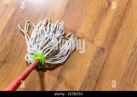 il punto di vista del mop di corda sta pulendo il laminato di legno pavimento a casa Foto Stock