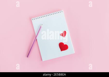 Notebook con pagina vuota, matita e cuori rossi su sfondo rosa. Disposizione piatta. Posiziona per il testo. Foto Stock