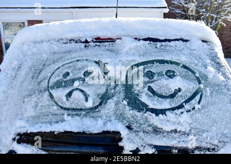 primo piano della schermata dell'auto coperta di neve con due volti emoji attratti dal ghiaccio, uno felice e uno triste. fuori in un freddo giorno di sole inverno Foto Stock