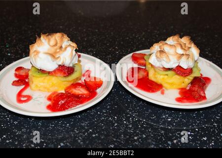 Primo piano di delizioso dolce meringa con fragole, kiwi e ananas. Piatto di alta frutta accatastato su un piatto di cina poggiato su kit nero Foto Stock