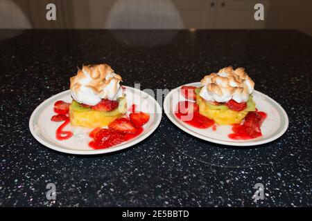 Primo piano di delizioso dolce meringa con fragole, kiwi e ananas. Piatto di alta frutta accatastato su un piatto di cina poggiato su kit nero Foto Stock