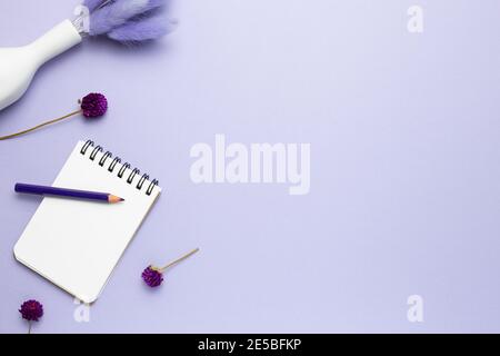 Taccuino, matita colorata, fiori secchi su sfondo viola. Posa piatta, vista dall'alto, spazio per la copia Foto Stock