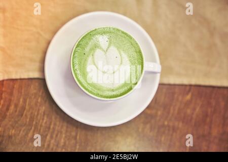 Tazza di latte matcha su sfondo di legno e un tovagliolo beige in un caffè con spazio per le copie. Foto di alta qualità Foto Stock