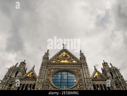 Alta façade della Cattedrale di Siena (Cattedrale Metropolitana di Santa Maria Assunta) contro un cielo sovrastato, Toscana, Italia Foto Stock