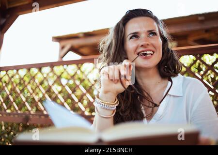 donna elegante e raffinata in camicia bianca con libro e occhiali nel patio dell'hotel. Foto Stock