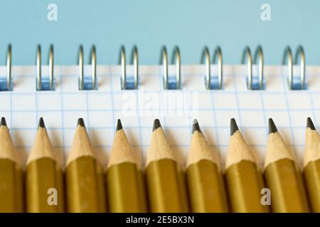 Concetto di istruzione, matite semplici si trovano su un notebook in una gabbia da vicino, profondità di campo poco profonda, sfondo blu Foto Stock