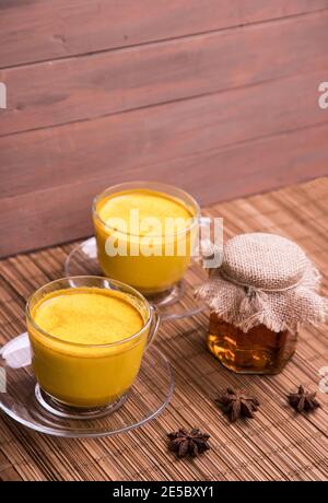 Tazze di latte dorato e un vasetto di miele su un tappetino di paglia. Bevanda di disintossicazione vegana asiatica alla moda fatta con latte di mandorle e curcuma. Foto Stock