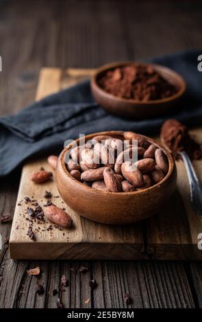 Snack sano, fagioli di cacao non tostati superfood in una ciotola di legno decorata con cacao in polvere Foto Stock