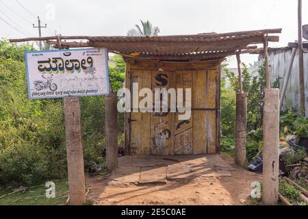 Nandakeshwar, Karnataka, India - 7 novembre 2013: Officina di riparazione del motociclo in legno dilapidato sotto il cielo d'argento. Verde fogliame intorno. Foto Stock