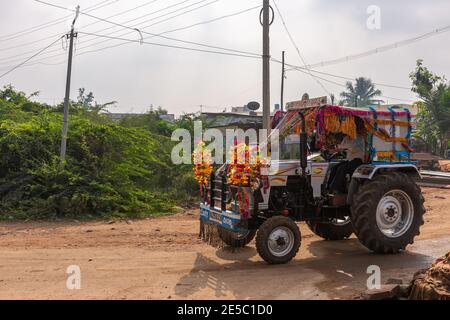 Nandakeshwar, Karnataka, India - 7 novembre 2013: Trattore su strada sterrata sport leis di fiori multipli per Diwali sotto il cielo d'argento con fogliame verde in Foto Stock