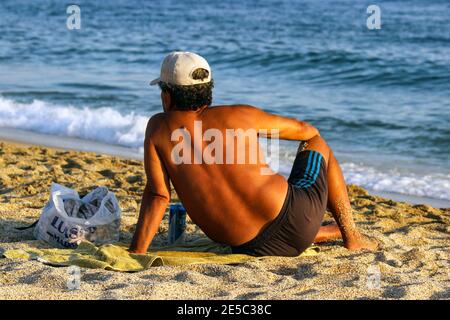 Uomo locale che si crogiolava al sole della sera alla spiaggia di Damlataş ad Alanya, Turchia Foto Stock