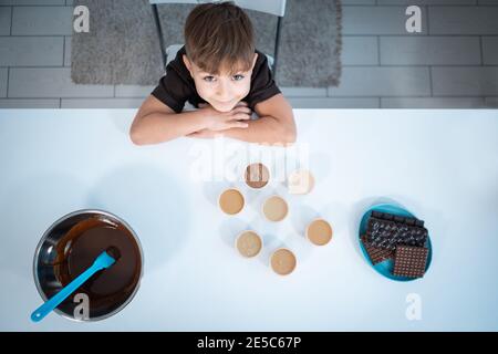 vista dall'alto di un bambino sorridente che fa barrette di cioccolato o dolci cucina a casa Foto Stock