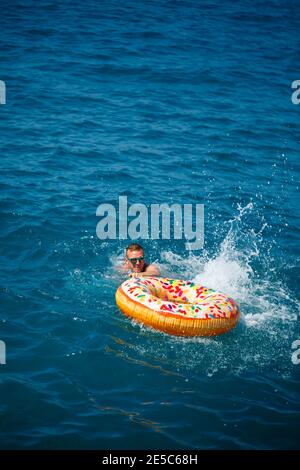 Un uomo galleggia su un anello gonfiabile in mare con acqua blu. Vacanza al mare in una giornata di sole. Concetto di vacanza in Turchia Foto Stock