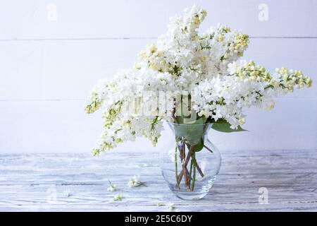 Bouquet lilla bianco in vaso di vetro su tavolo di legno. Primavera rami di lilla fiore festoso bouquet di fiori con spazio copia. Foto Stock