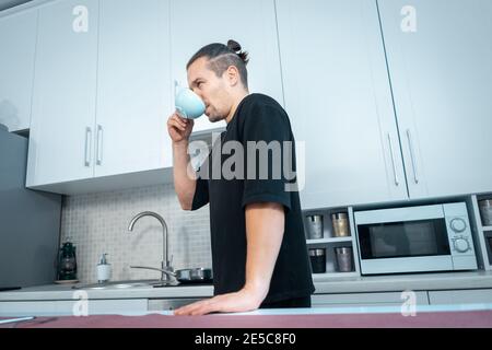 giovane uomo attraente bere tè caldo delizioso o caffè sopra cucina moderna Foto Stock