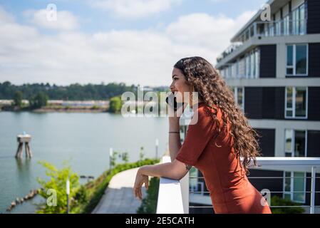 Felice giovane donna che parla al telefono sul balcone della città con fiume Foto Stock