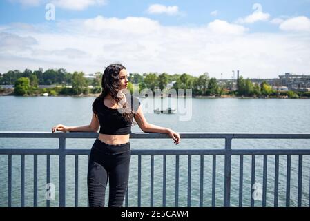 Giovane donna appoggiata sulla ringhiera con fiume e barca dentro sfondo Foto Stock