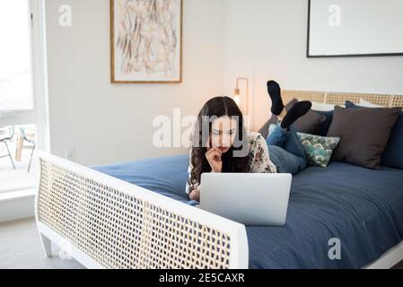 Giovane donna giaceva sul letto guardando al laptop Foto Stock