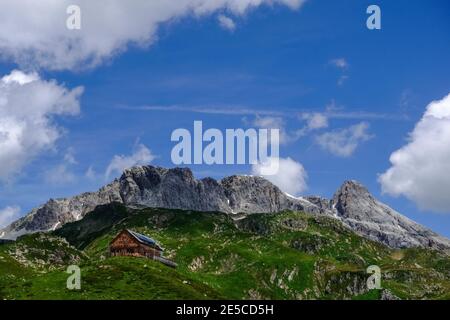 casa di legno su una collina verde e meravigliose montagne rocciose con cielo blu Foto Stock