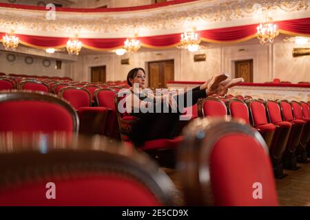 Ballerina femminile seduta in auditorium e in attesa di esibizione in un teatro vuoto Foto Stock