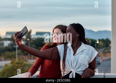 Due giovani donne stanno prendendo un auto-ritratto con il loro telefono al tramonto Foto Stock