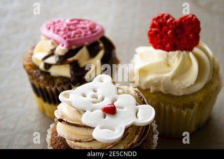 Primo piano di cupcake di butterscotch con glassa di crema bianca e marrone con fondente di orsacchiotto bianco e cuore rosso per la giornata di San Valentino, con marmo Foto Stock