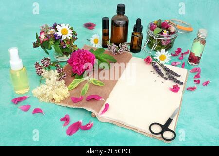 Preparazione di olio essenziale per l'uso in aromaterapia e medicina naturale a base di erbe con fiori estivi e erbe con notebook di canapa, contagocce e bottiglie di olio. Foto Stock