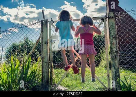 Vista posteriore di due ragazze che si arrampicano su una recinzione metallica, Polonia Foto Stock