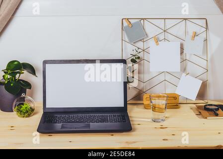 Ambiente di lavoro moderno - scrivania in legno con schermo vuoto bianco mockup per computer portatile, mood board con note e foto in tessere, piante verdi nello spazio di lavoro in ufficio domestico Foto Stock